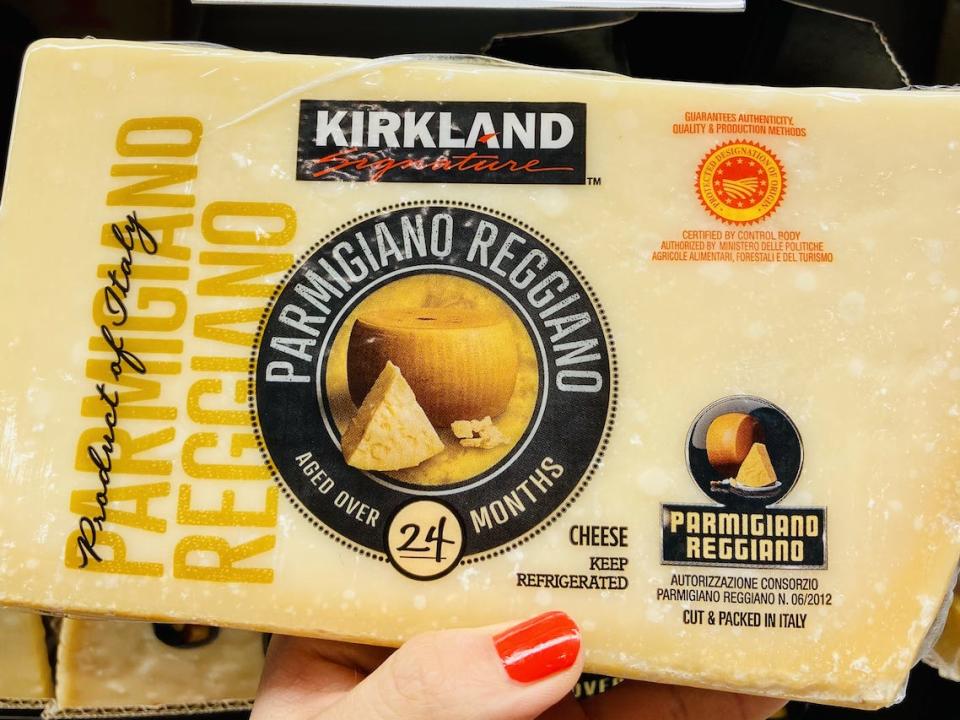 A hand holding a block of Kirkland parmigiano reggiano in the cheese section