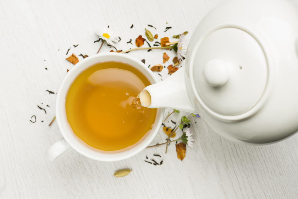 pouring tea with teapot into cup on white table for natural hair rinse