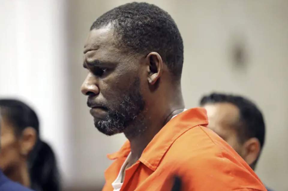 R. Kelly's side profile in an orange jumpsuit in a courtroom