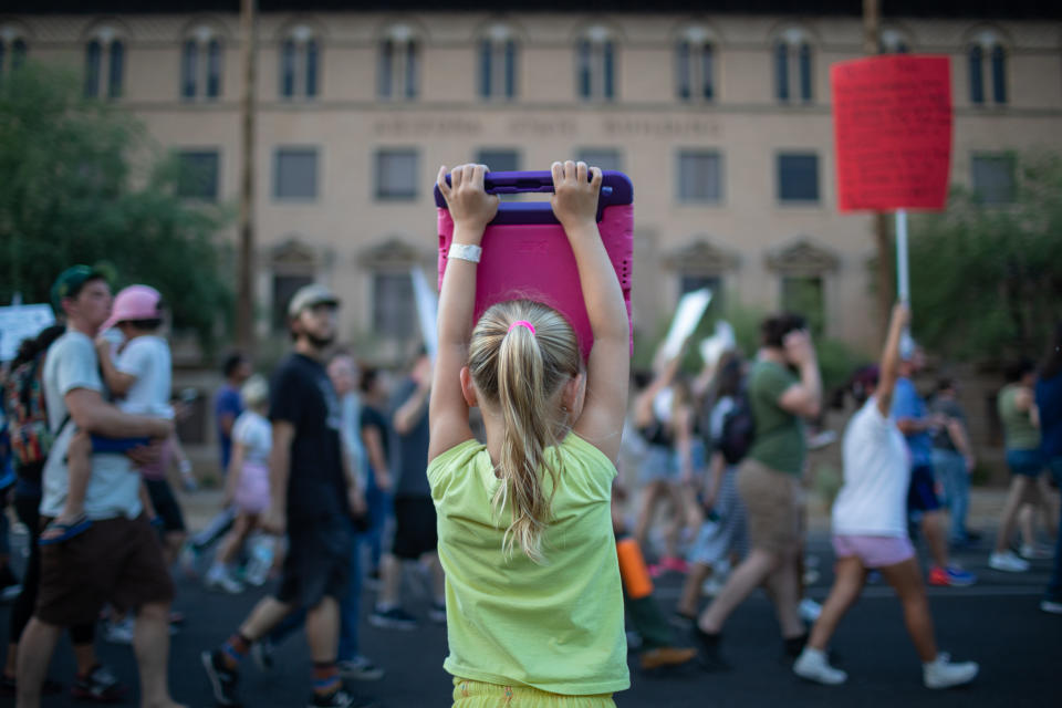 Six-year-old Reagan Burback, in lime-green shirt, holds up a pink iPad above her head.