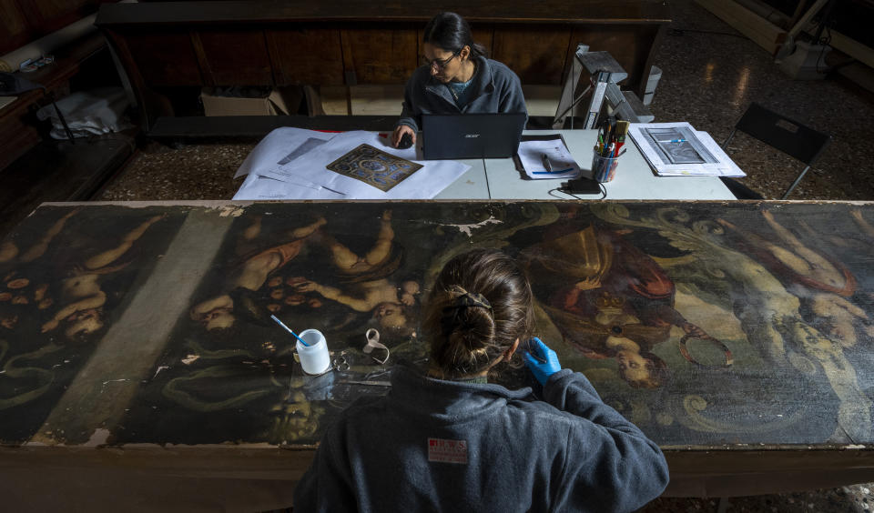 Restorers Annalisa Tosatto, top, and Alice Chiodelli work at the conservation and study of ' The reward and a pair of putti', a 1590 painting by Venetian Renaissance artist Andrea Michieli known as Andrea Vicentino in a makeshift laboratory set up in the Venetian Doge's private chapel inside Palazzo Ducale in Venice, northern Italy, Wednesday, Dec. 7, 2022. The 93x330 centimeters (approximately 36.6x130 inches) canvas was adorning the Grimani's Hall in the Doge's apartments of Palazzo Ducale. (AP Photo/Domenico Stinellis)