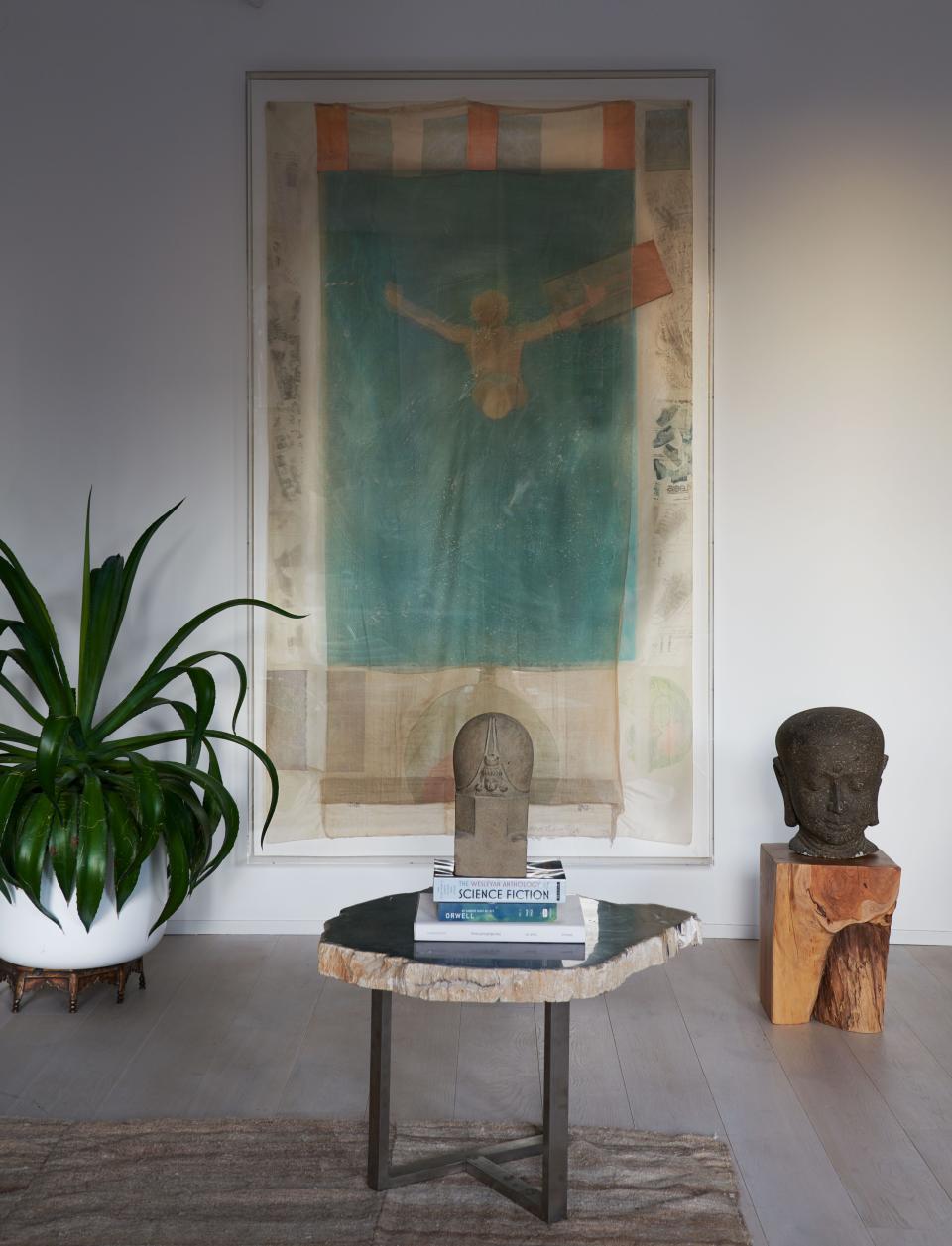 A painting by Robert Rauschenberg hangs behind a petrified oak side table topped with a contemporary Javan stone head.