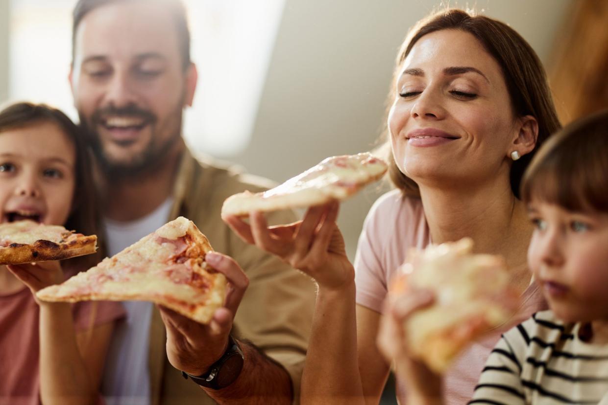 Happy woman enjoying while eating pizza with her family at home.
