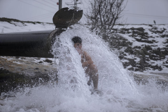 An Israeli man sits under hot water coming out of a pipe from a drilling project which exposed a subterranean hydrothermal spring, at a snow-covered reservoir next to Mount Bental in the Israeli-controlled Golan Heights, near the Israeli border with Syria Wednesday, Jan. 19, 2022. Snow fell in parts of the Middle East as a winter storm swept through the region. (AP Photo/Ariel Schalit)