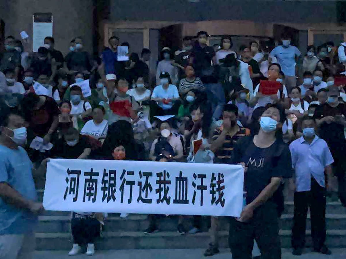 People hold banners and chant slogans stage a protest at the entrance to a branch of China's central bank in Zhengzhou in central China's Henan Province (AP)