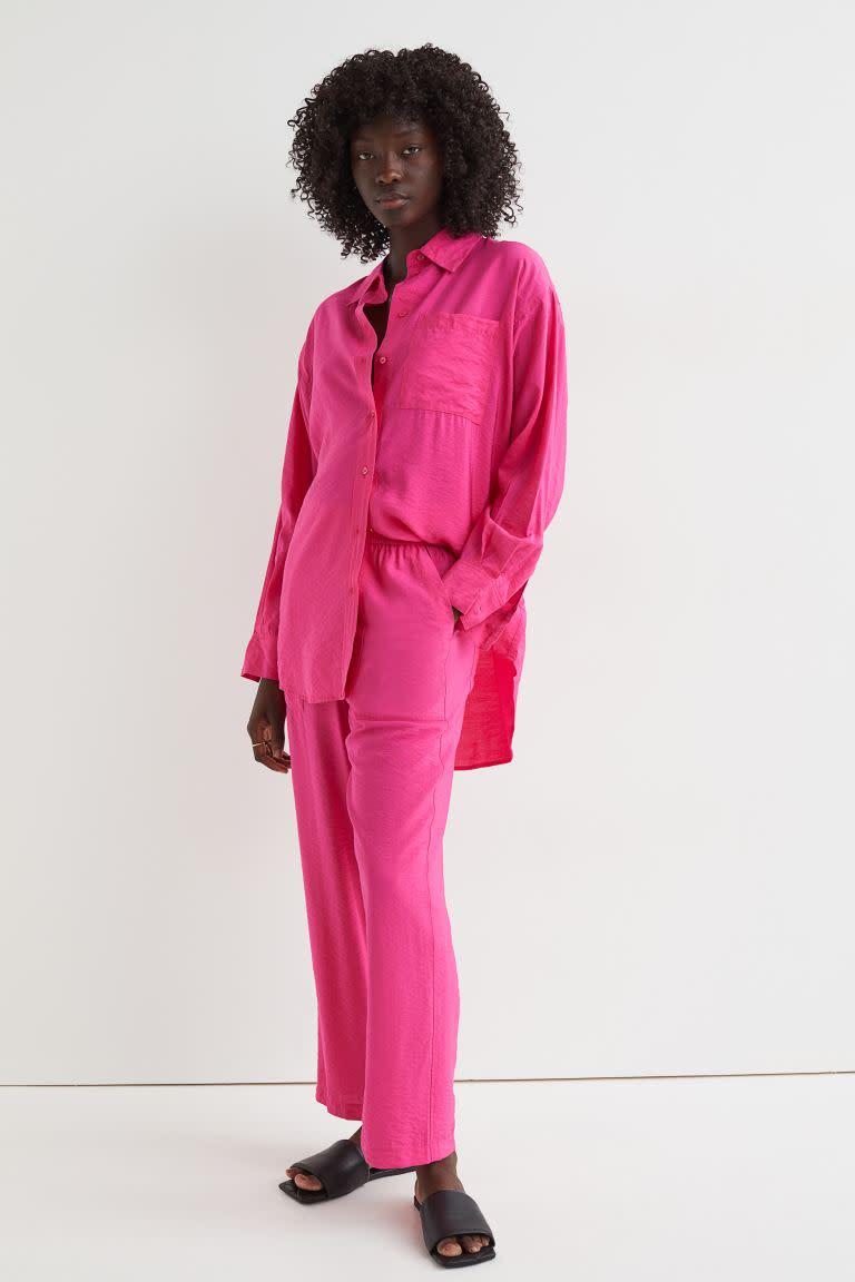 A model wears hot pink Straight Pull On Pants, $39.99, from H&M, with matching loose long shirt and black slide sandals.