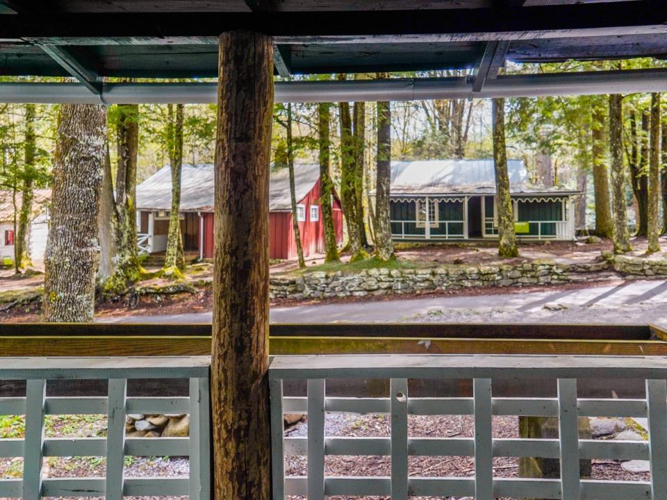 A view of cabins in the trees from a front porch with a log pillar to the left of the center