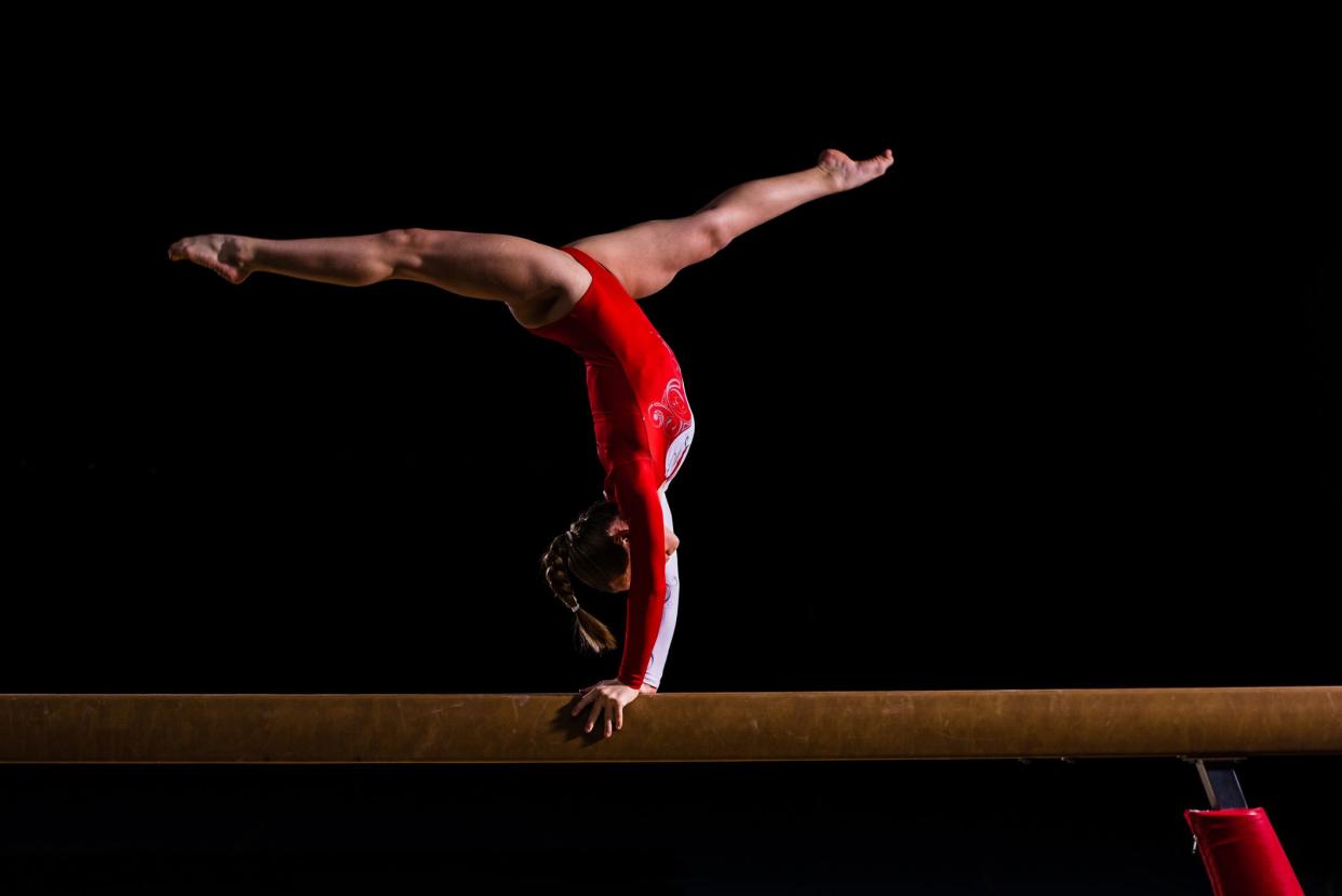 Young woman balancing on balance beam in sports hall.