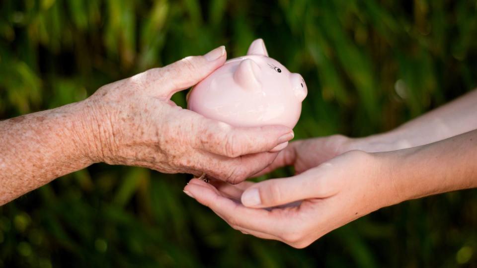 Gros plan de la main d'une femme âgée qui transmet une tirelire à une jeune femme