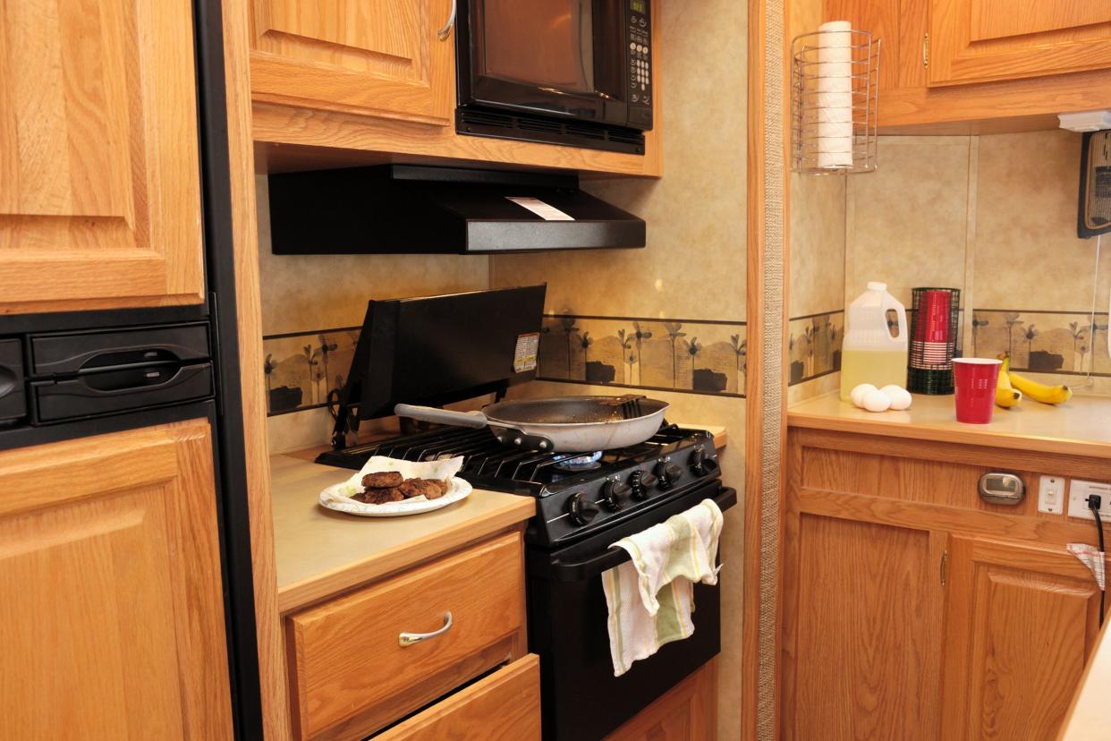 cooking sausage on stove in spacious RV kitchen with wooden cabinets with other food items on counter