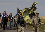 FILE In this file photo taken on Tuesday, July 22, 2014, A pro-Russian rebel holds a gun passing by plane wreckage as members of the OSCE mission to Ukrainearrive for a media briefing at the crash site of Malaysia Airlines Flight 17, near the village of Hrabove, eastern Ukraine. International investigators on Wednesday, June 19, 2019 announced murder charges against three Russians, including a prominent separatist rebel commander, and one Ukrainian, for their alleged roles in blowing a Malaysia Airlines passenger jet out of the sky five years ago, a shocking attack that killed all 298 people on board. (AP Photo/Vadim Ghirda, File)