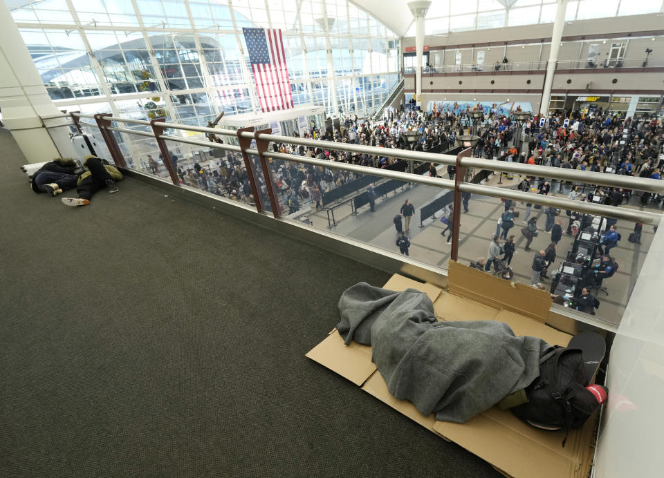 Travelers sleep as fellow travelers queue up to pass through the south security checkpoint in Denver International Airport after a winter storm swept over the country packing snow combined with Arctic cold, which created chaos for people trying to reach their destinations before the Christmas holiday, Friday, Dec. 23, 2022, in Denver. Forecasters predict that warmer weather will be on tap for the week ahead. (AP Photo/David Zalubowski)