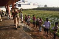 A security officer wearing a face shield as a protective measure against the coronavirus stands guard as voters stand in a queue at a polling station, during the first phase of state elections at Paliganj, in the eastern Indian state of Bihar, Wednesday, Oct. 28, 2020. With an overall declining coronavirus positive trend, Indian authorities decided to hold the first state legislature election since the outbreak of COVID-19. People began voting Wednesday in the country’s third largest state Bihar with of a population of about 122 million people. (AP Photo/Aftab Alam Siddiqui)