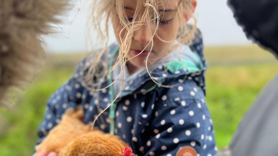 Amanda Owen's daughter with a chicken in a field