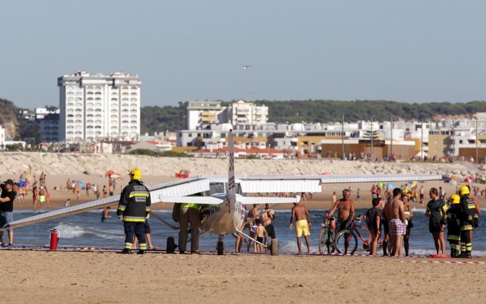 Onlookers watch as firefighters inspect a plane that crash landed on Sao Joao beach in Costa da Caparica - Credit: AP