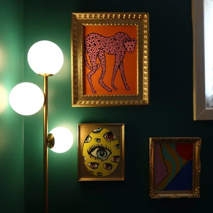 Reviewer's photo of the floor lamp focusing on the three globes at the top, set against a dark green wall with framed art