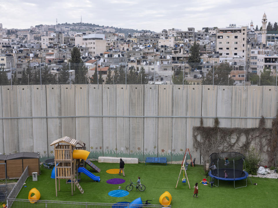 Jewish settlers who live in the Rachel's Tomb compound enjoy their playground located next to a section of Israel's concrete barrier, separating them from the West Bank city of Bethlehem in the background, Tuesday, March 8, 2022. Twenty years after Israel decided to built its controversial separation barrier amid a wave of Palestinian attacks, it remains in place, even as Israel encourages its own citizens to settle on both sides and admits tens of thousands of Palestinian laborers. (AP Photo/Oded Balilty)