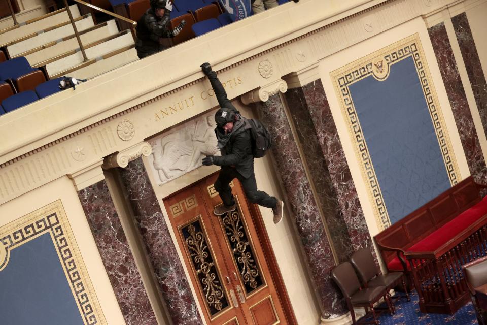 A Trump supporter hangs from the balcony in the Senate chamber.