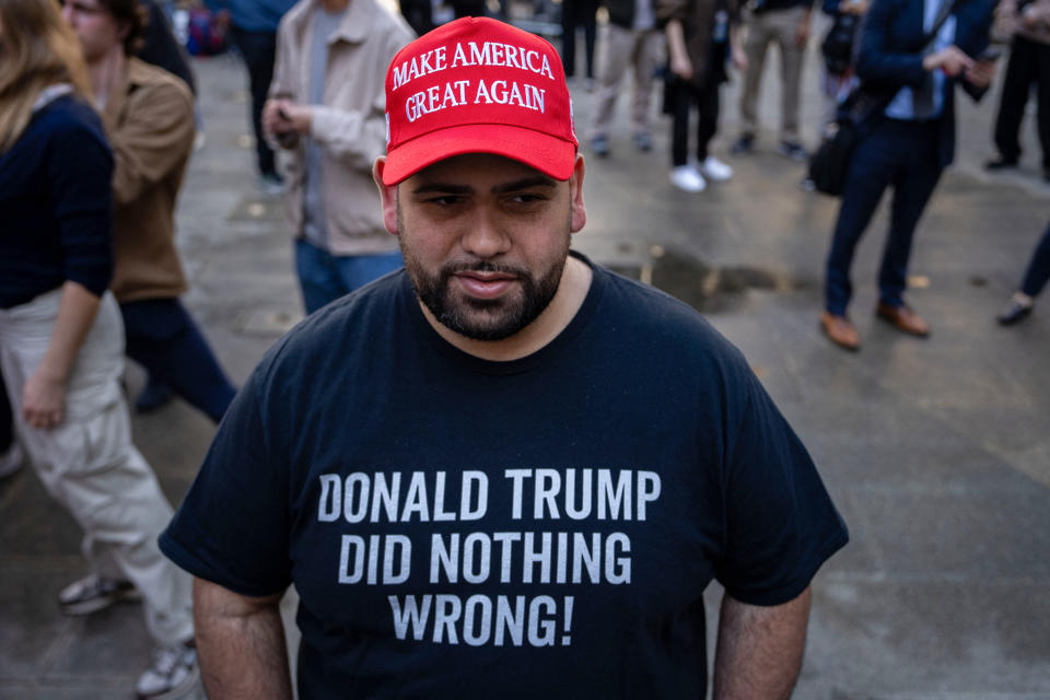 Man in MAGA hat and shirt with text supporting Donald Trump, in a crowd