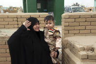 In this Wednesday, Feb. 15, 2017, the widow of Hamza Finjan, who was killed fighting Islamic State militants in Mosul, holds their son Ammar Hamza wearing a tiny replica of a military uniform as she visits the grave of her husband in Wadi al-Salam, or "Valley of Peace" cemetery which contains the graves of security forces and militiamen killed from fighting with Islamic State group militants, in Najaf, 100 miles (160 kilometers) south of Baghdad, Iraq. Hundreds of Iraqi soldiers are estimated to have died in the fight for Mosul so far, but the Iraqi government does not release official casualty reports, a move that many Iraqis view as disrespectful of their sacrifice. (AP Photo/ Khalid Mohammed)