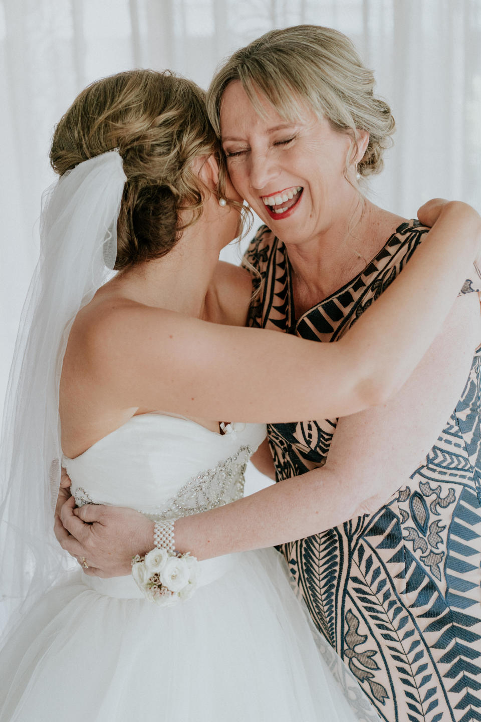 The bride and her mother share a joyful embrace. On the left is Agnew in a white ball gown and veil, with her head turned away from the camera. On the right is Agnew's mother with a big smile on her face, wearing a tan-and-navy patterned dress. (Photo: <a href="https://www.jamesday.com.au/" target="_blank">James Day Photography</a>)