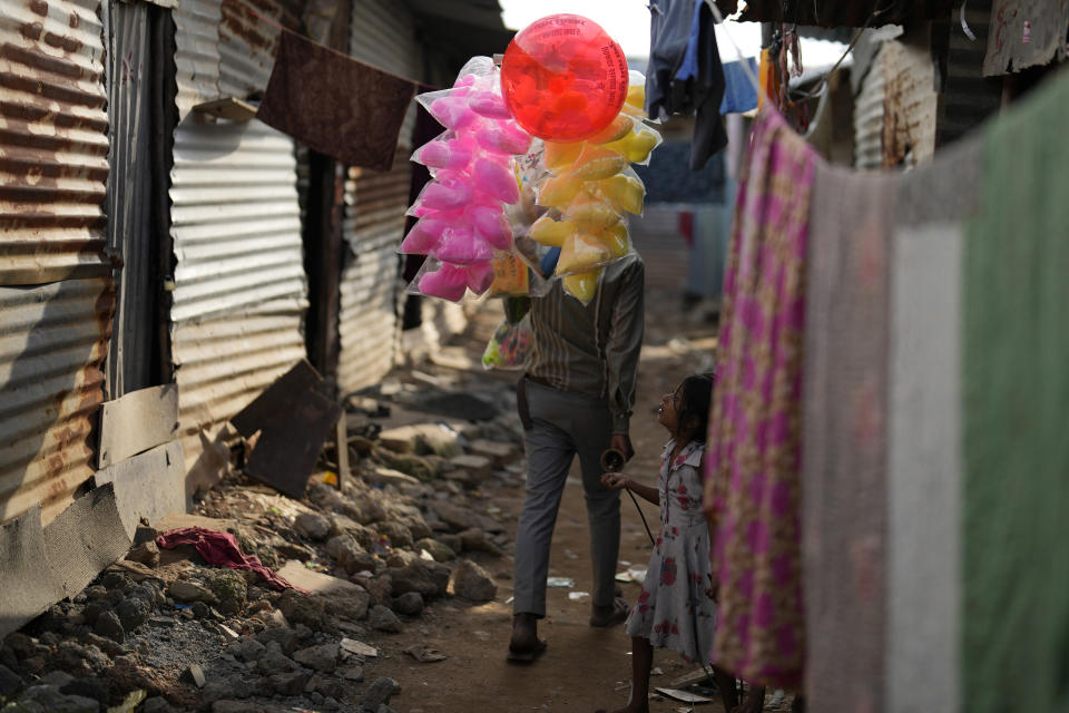 A girl looks at a man selling colorful candies as he walks through the narrow lanes of a poor community in Bengaluru, India, Tuesday, July 19, 2022. In this community, most people are from Assam state, many forced to migrate because of climate change and dreaming of a better future. (AP Photo/Aijaz Rahi)