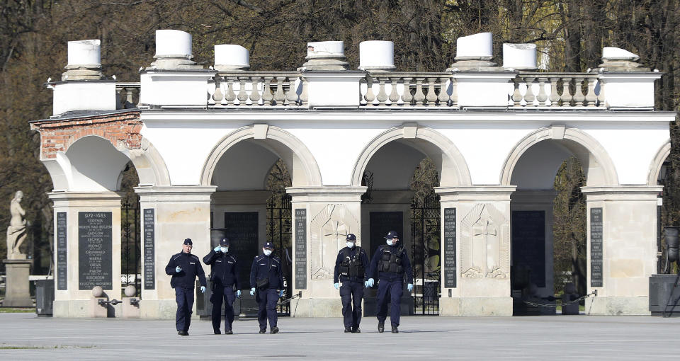 Police in masks against the coronavirus spread watches over a scaled-down observance in memory of the late President Lech Kaczynski, the twin brother of Poland's ruling conservative party leader Jaroslaw Kaczynski, and of 95 other prominent Poles who were killed in a plane crash in Russia 10 years ago, in Warsaw, Poland, on Friday, April 10, 2020. The observances were scaled down to just Kaczynski and a few people and no crowd under social distancing regulations against the coronavirus spread. The new coronavirus causes mild or moderate symptoms for most people, but for some, especially older adults and people with existing health problems, it can cause more severe illness or death.(AP Photo/Czarek Sokolowski)