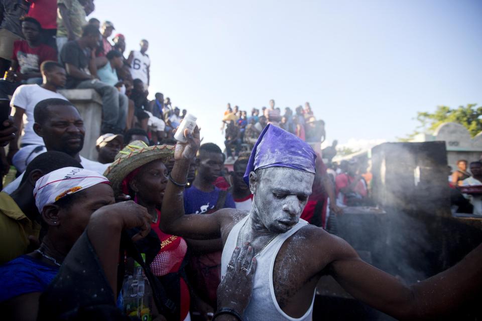In this Nov. 1, 2018 photo, voodoo believers who are supposed to be possessed with Gede spirit perform rituals in the middle of Baron Samedi's tomb during the annual Voodoo festival Fete Gede at Cite Soleil Cemetery in Port-au-Prince, Haiti. Every year, during the celebration, they paint their faces with white powder, wear the loas' clothes, travel the narrowly pathways through the shanty town and go to cemeteries to pay tribute to the spirits.( AP Photo/Dieu Nalio Chery)
