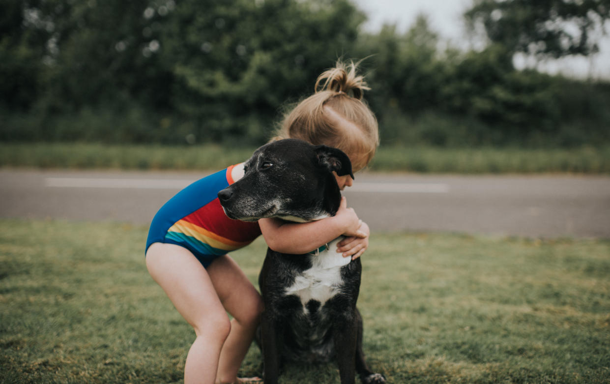 Cute young girl hugs black dog.