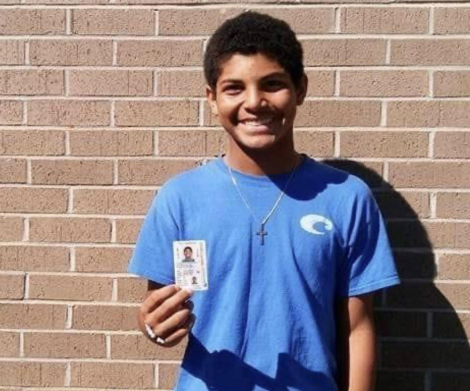 Keegan Johnson, stands against a brick wall, smiling as he holds his driver's license.