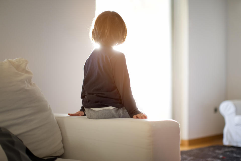 A small boy sits on the arm of a couch in a house