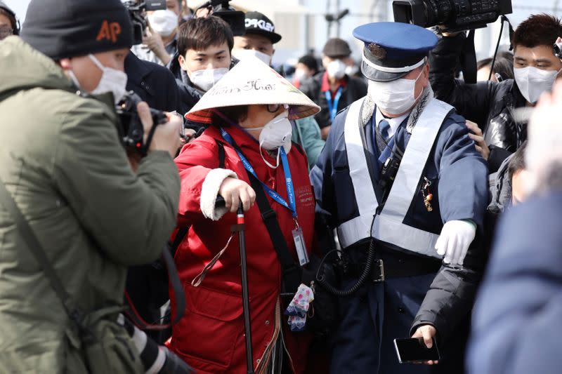 A police officer escorts a passenger away from the media as she walks out from the cruise ship Diamond Princess at Daikoku Pier Cruise Terminal in Yokohama