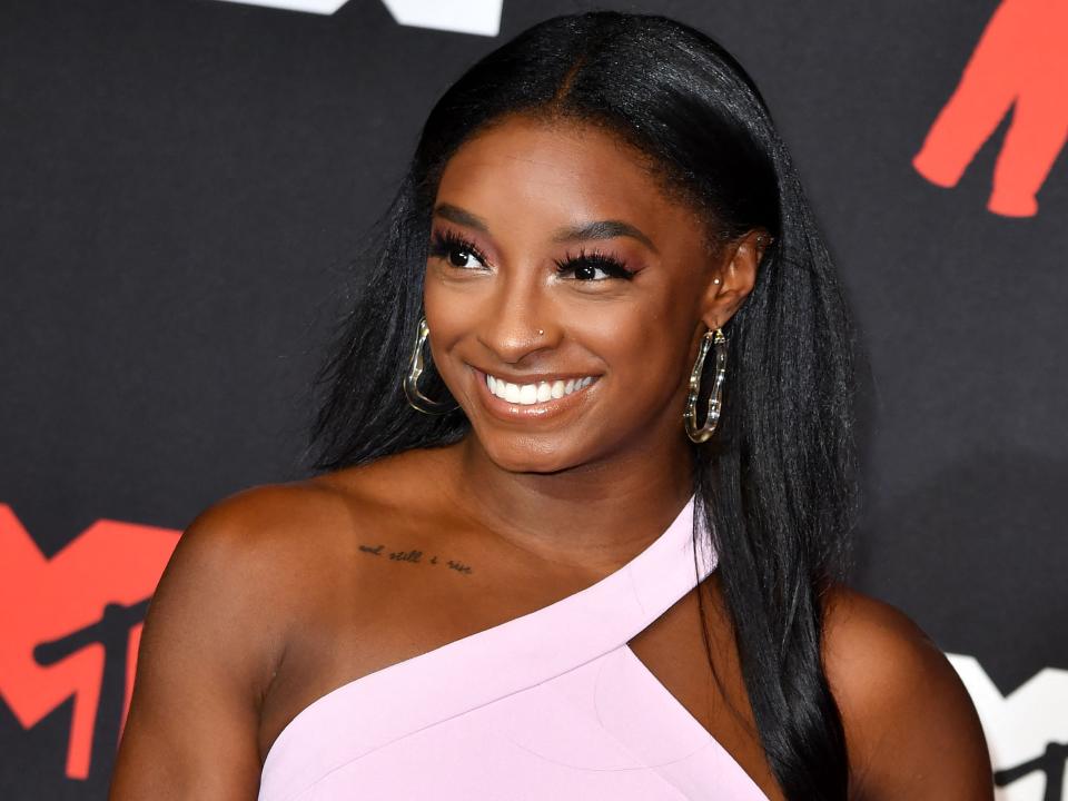 Simone Biles smiles in a pink, one-shoulder dress