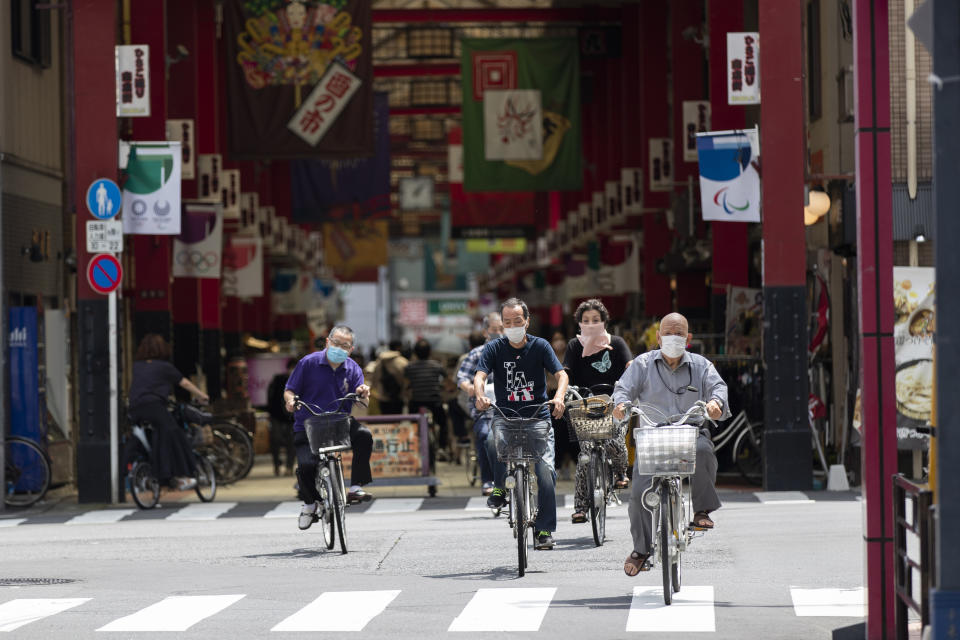 People wearing face masks ride bicycles as they cross an intersection near a shopping street in Tokyo on Thursday, July 15, 2021. (AP Photo/Hiro Komae)