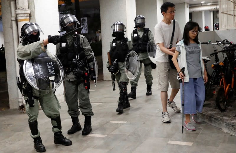 People walk past riot police dispering protesters outside a shopping mall in Tai Po in Hong Kong
