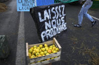 Apples are made available next to a poster reading " Let us produce" as farmers block highway, Thursday, Feb.1, 2024 in Argenteuil, north of Paris. France's two major farmers unions announced Thursday their decision to suspend protests and lift road blockades across the country, in a dramatic development shortly after the French prime minister unveiled a new set of measures they see as "tangible progress." Farmers have been protesting for days across the country to denounce low wages, heavy regulation and unfair competition from abroad. (AP Photo/Michel Euler)