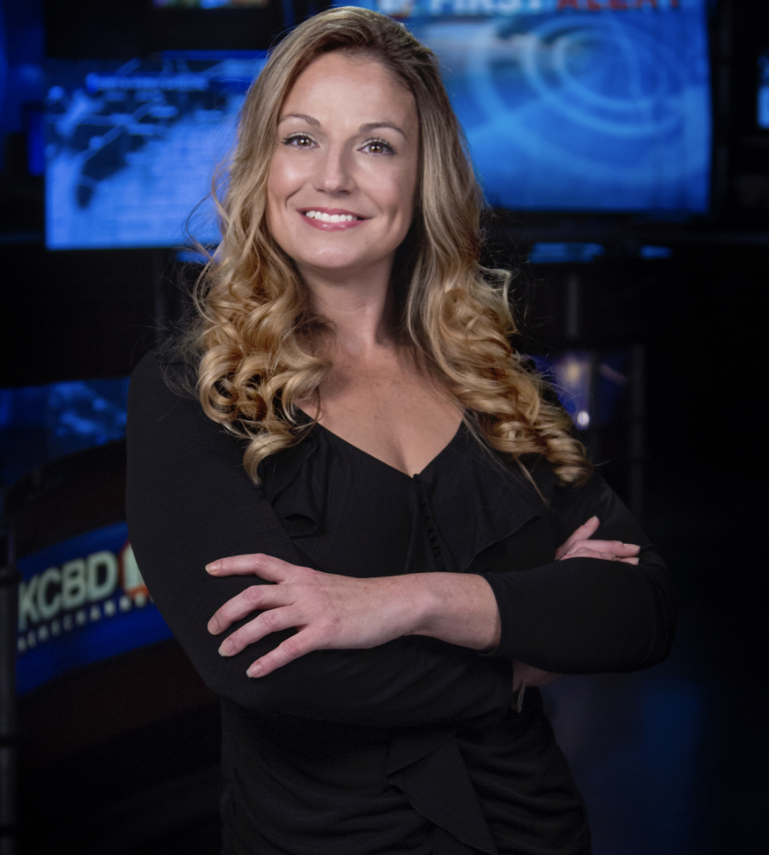 Kelly Plasker folds her arms and poses for a professional photo shoot in a TV studio.