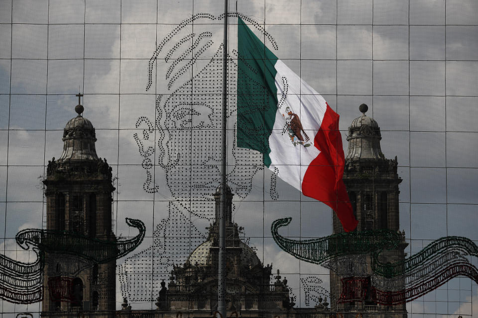 En esta imagen, tomada el 15 de septiembre de 2020, una instalación de luces con la imagen de Leona Vicario cuelga ante la Catedral Metropolitana antes del "grito", en la Plaza del Zócalo, en Ciudad de México. En lugar de ante la multitud que solía llenar el Zócalo por la fiesta, en este Día de la Independencia marcado por el coronavirus el presidente del país, Andrés Manuel López Obrador, se dirigirá a una plaza vacía para el tradicional "Grito de Dolores", que conmemora el llamado a las armas realizado en 1810 por el sacerdote Miguel Hidalgo, que inició la lucha para independizarse de España. (AP Foto/Rebecca Blackwell)