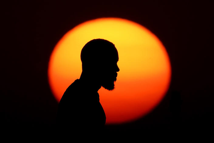 A man watches the sunset in a park at the close of a hot summer day, Monday, Aug. 1, 2022, in Kansas City, Mo. Sunsets in the midwest have been more vibrant than usual lately because of smoke from western wildfires in the atmosphere. (AP Photo/Charlie Riedel)
