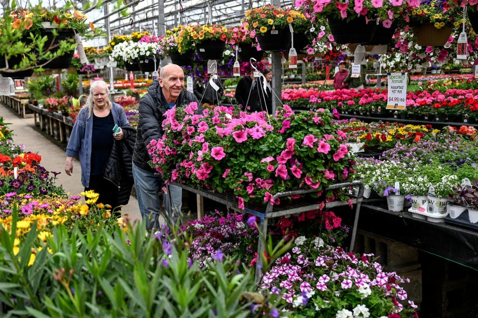 David Smitley, right, pushes a cart of hanging flower baskets that were his wife Dottie Best's, left, early Mother's Day present at Horrocks Farm Market Saturday, April 30, 2022, in Delta Township.