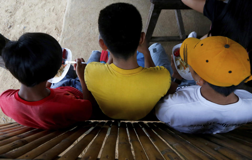 In this Jan. 27, 2019 photo, three boys have a snack at a beach resort in Talustusan on Biliran Island in the central Philippines. Since December 2018, the small village has been rocked by controversy after about 20 boys and men, including these three, accused their Catholic parish priest Father Pius Hendricks of years of alleged sexual abuse. (AP Photo/Bullit Marquez)