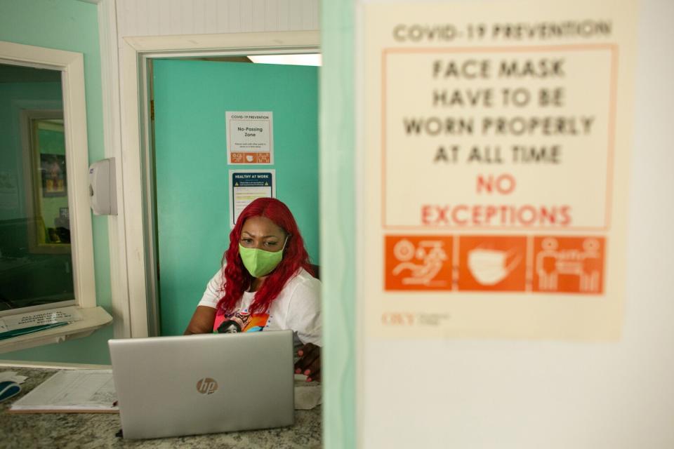 A woman wearing a mask sits in front of a laptop at a desk