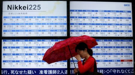 FILE PHOTO - A woman holding an umbrella walks past an electronic board showing Japan's Nikkei 225 outside a brokerage in Tokyo, July 8, 2015. REUTERS/Toru Hanai