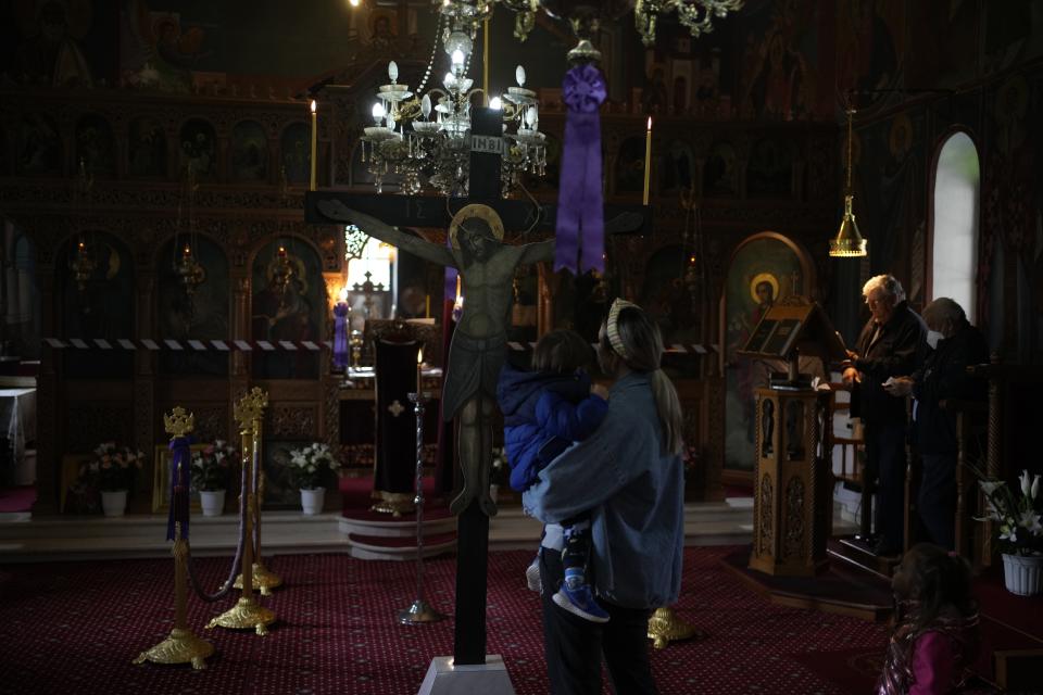 Christina Anastasopoulou holds her son Giorgos-Filippos as his sister Amelia stands next to them as they attend a liturgy in Agios Georgios church, in Myrodafni village, Epirus region, northwestern Greece, on Holy Friday, April 22, 2022. For the first time in three years, Greeks were able to celebrate Easter without the restrictions made necessary by the coronavirus pandemic. (AP Photo/Thanassis Stavrakis)