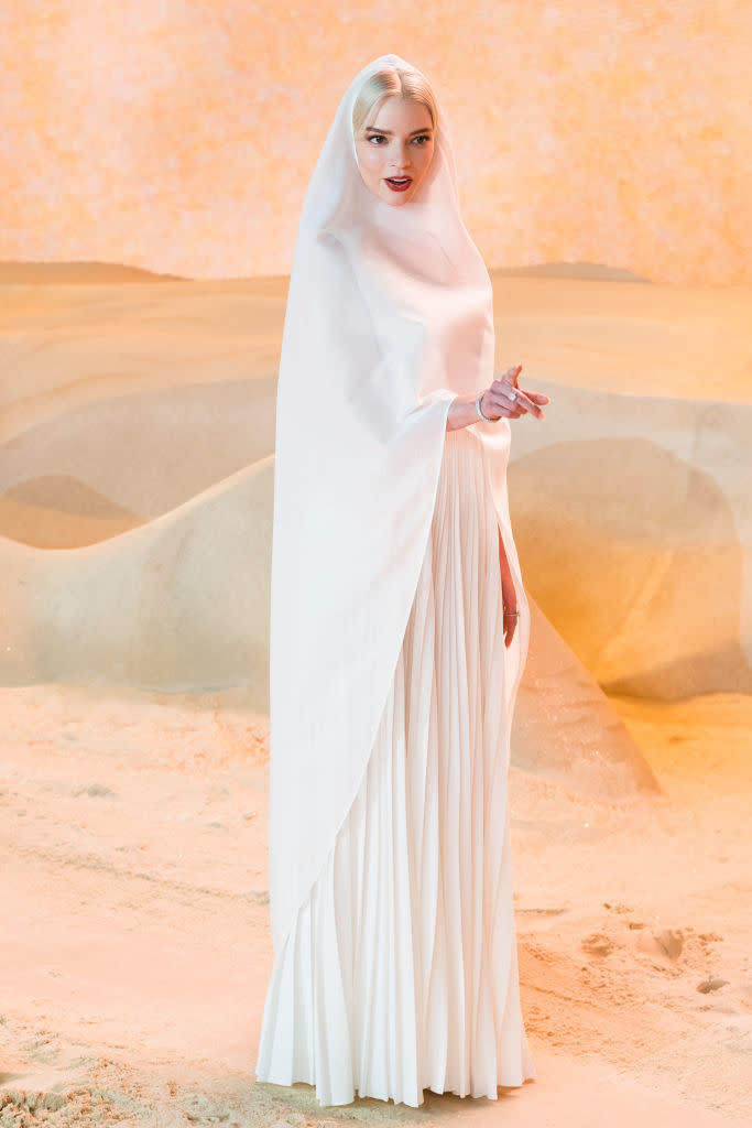 Woman in elegant white draped gown and sheer headscarf posing for a photoshoot