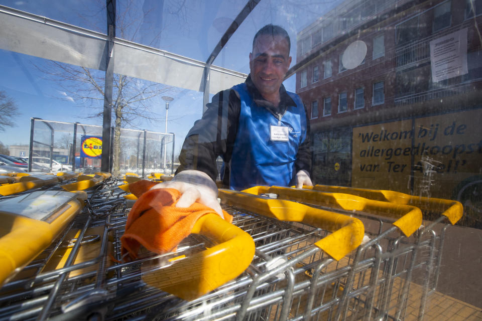 Raffat Altekrete is battling the coronavirus one shopping cart at a time as he uses a disinfecting spray outside a supermarket in Ter Apel, north-eastern Netherlands, Tuesday, March 31, 2020. The Iraqi migrant, armed with latex gloves, a cleaning rag and a spray bottle of disinfectant is also aiming to express his gratitude and win hearts in a small Dutch community that hosts the Netherlands' biggest asylum seeker center. (AP Photo/Peter Dejong)