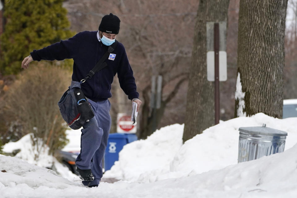 Postal carrier Josiah Morse steps carefully on a snowy sidewalk, Wednesday, Feb. 3, 2021, in Portland, Maine. The U.S. Postal Service's stretch of challenges didn't end with the November general election and tens of millions of mail-in votes. The pandemic-depleted workforce fell further into a hole during the holiday rush, leading to long hours and a mountain of delayed mail. (AP Photo/Robert F. Bukaty)