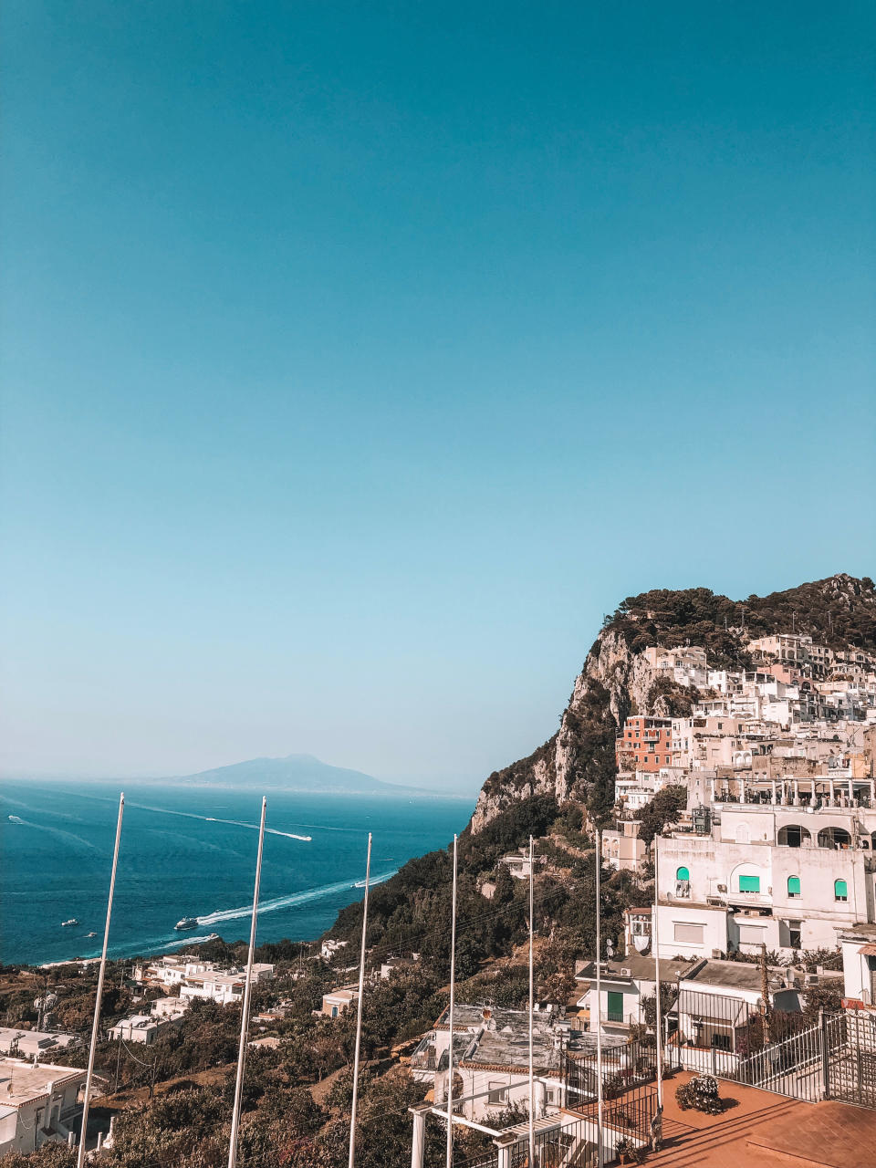 Mountains and cliffs of Capri leading to the ocean. Stacked buildings built into the side of the mountain with large terraces overlooking the view.