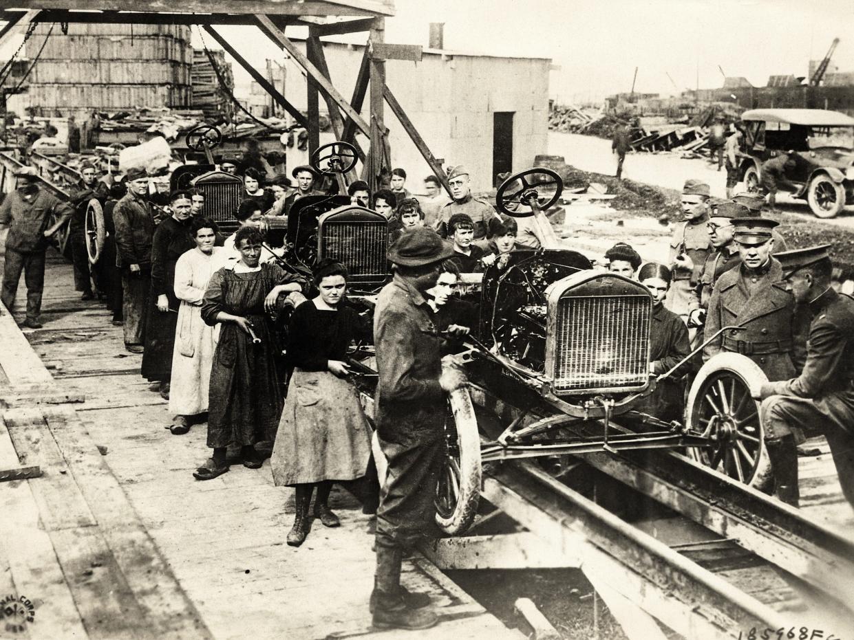 Picture shows women working on an early outdoor Ford assembly line, 1910.