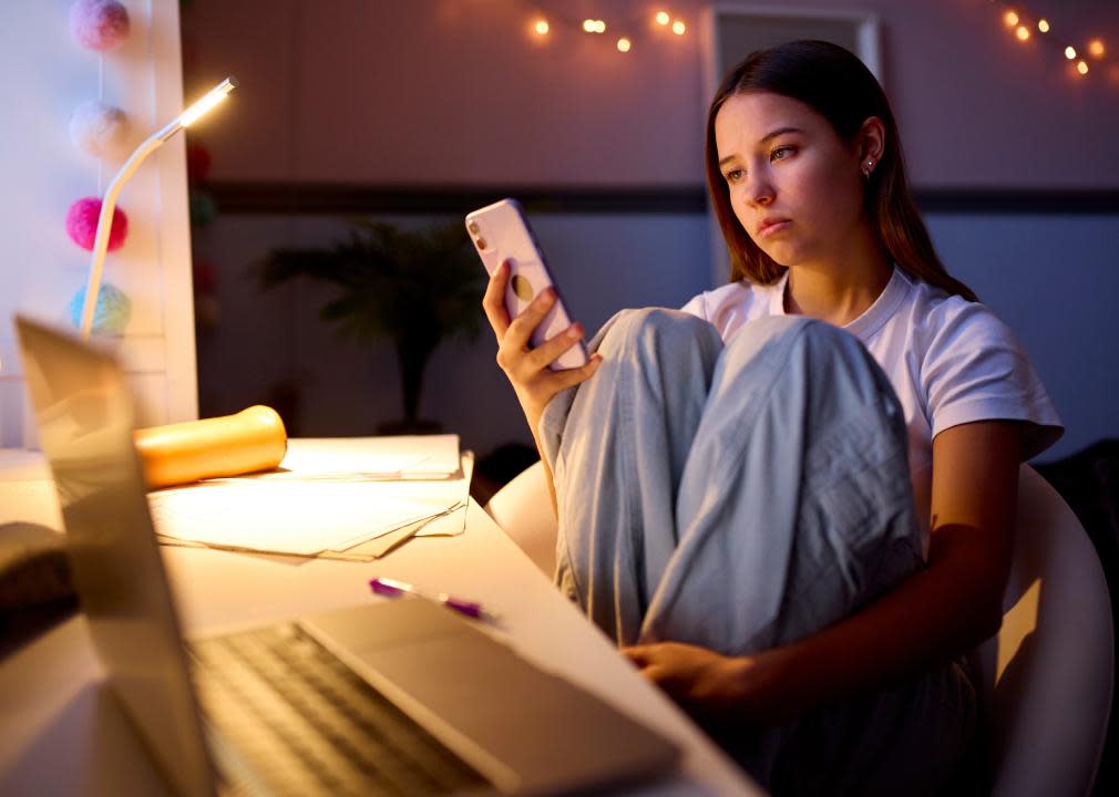 Teenage girl sitting at a desk looking at phone.